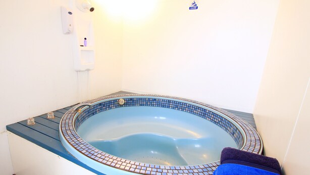 A small, round, blue-tiled hot tub with a blue towel on the side. - Golden Glow Motel (Rotorua)