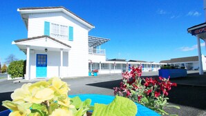 A white building with a blue door and balcony, surrounded by potted plants and flowers. - Golden Glow Motel (Rotorua)
