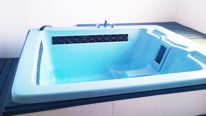 A rectangular hot tub with a tiled surround, a faucet, and a control panel. - Golden Glow Motel (Rotorua)