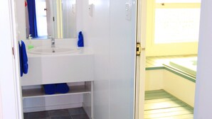 A bathroom with a white sink, mirror, and blue towels. There is a shower area with a glass door and a yellow wall. - Golden Glow Motel (Rotorua)