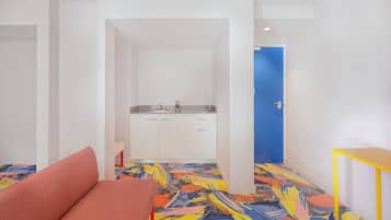 A compact room with a kitchenette, a sofa, and a colorful abstract-patterned floor.