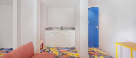 Habitación compacta con kitchenette, un sofá y un piso con un estampado abstracto y colorido.