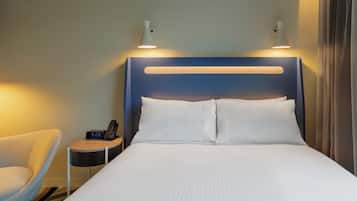 Habitación de hotel con cama, mesita de noche, lámpara, silla y un reloj.