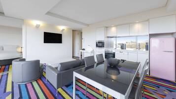 Una habitación de hotel moderna con sofá, una mesita de vidrio, zona de cocina y una alfombra colorida a rayas.