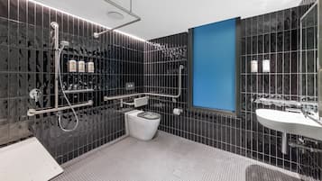 Un baño moderno con pared de azulejos negros, lavamanos blanco y zona de ducha.