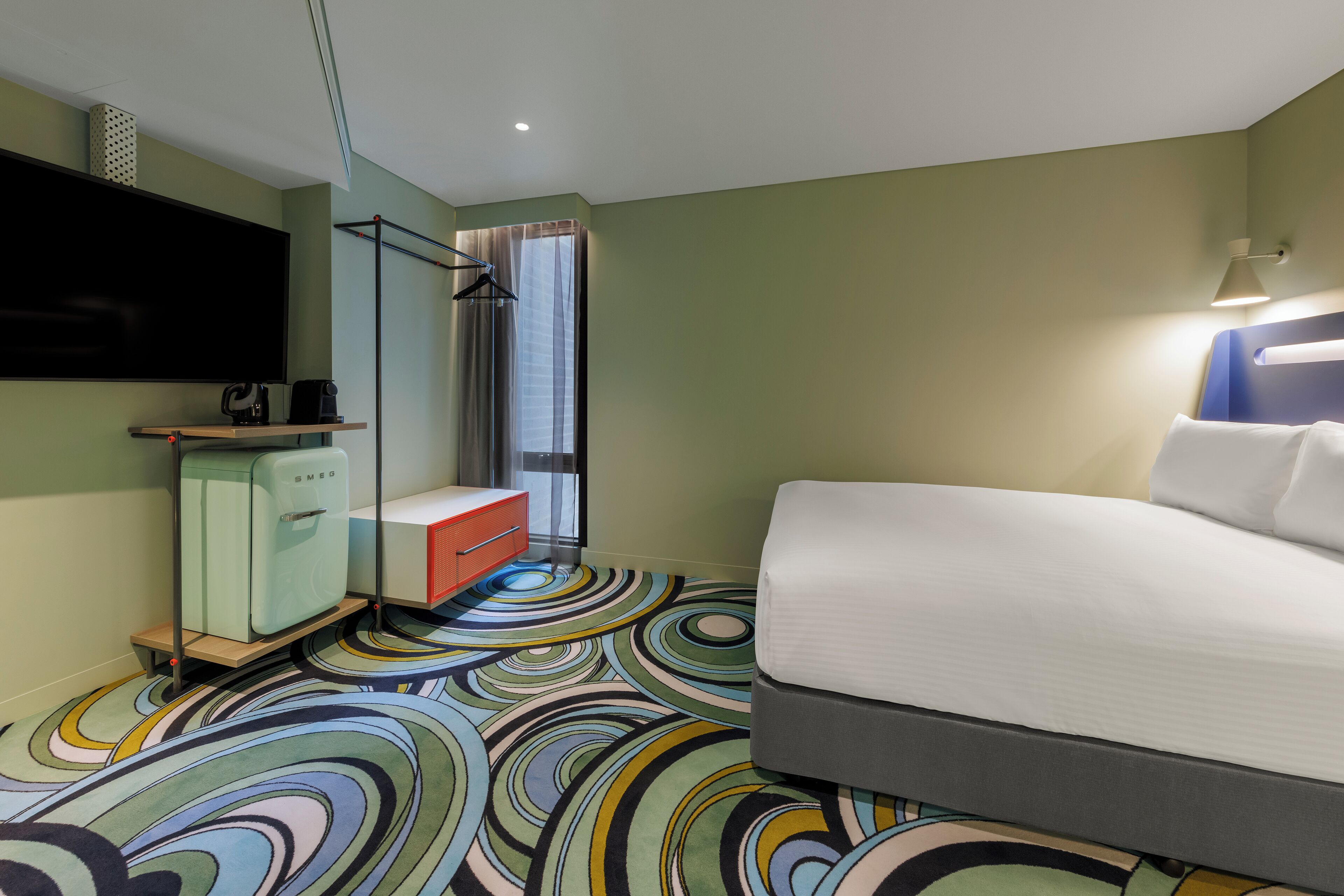 Habitación de hotel con cama, televisión, minibar, ducha y alfombra de colores.