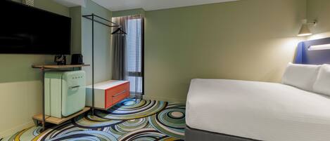 Una camera d'albergo con un letto, una TV, un minibar, una doccia e un tappeto colorato.
