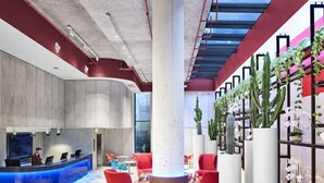 A modern lobby with a reception desk, colorful chairs, a central pillar, and a plant wall. - ADGE Hotel & Residences (Surry Hills)
