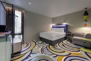 A hotel room with a bed, a sofa, a desk, and a colorful circular carpet.