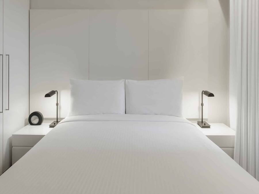 Een moderne slaapkamer met een groot bed, twee nachtkastjes en een bijzetmeubel.