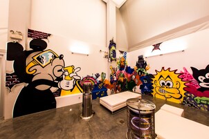Une pièce avec un mur couvert de graffitis, un lit, une table avec une bouteille d’eau et une poubelle.