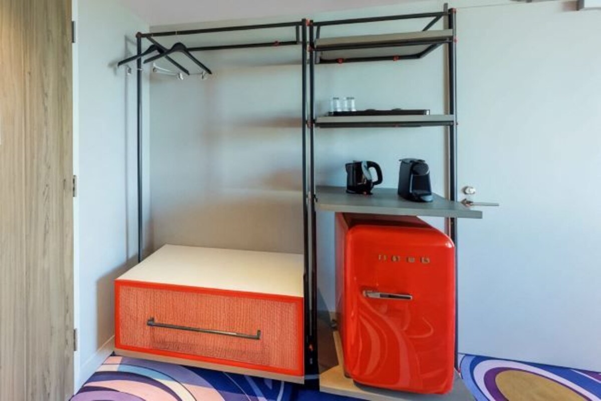 A compact room with a bunk bed, a small kitchenette with a coffee maker, and a storage unit.