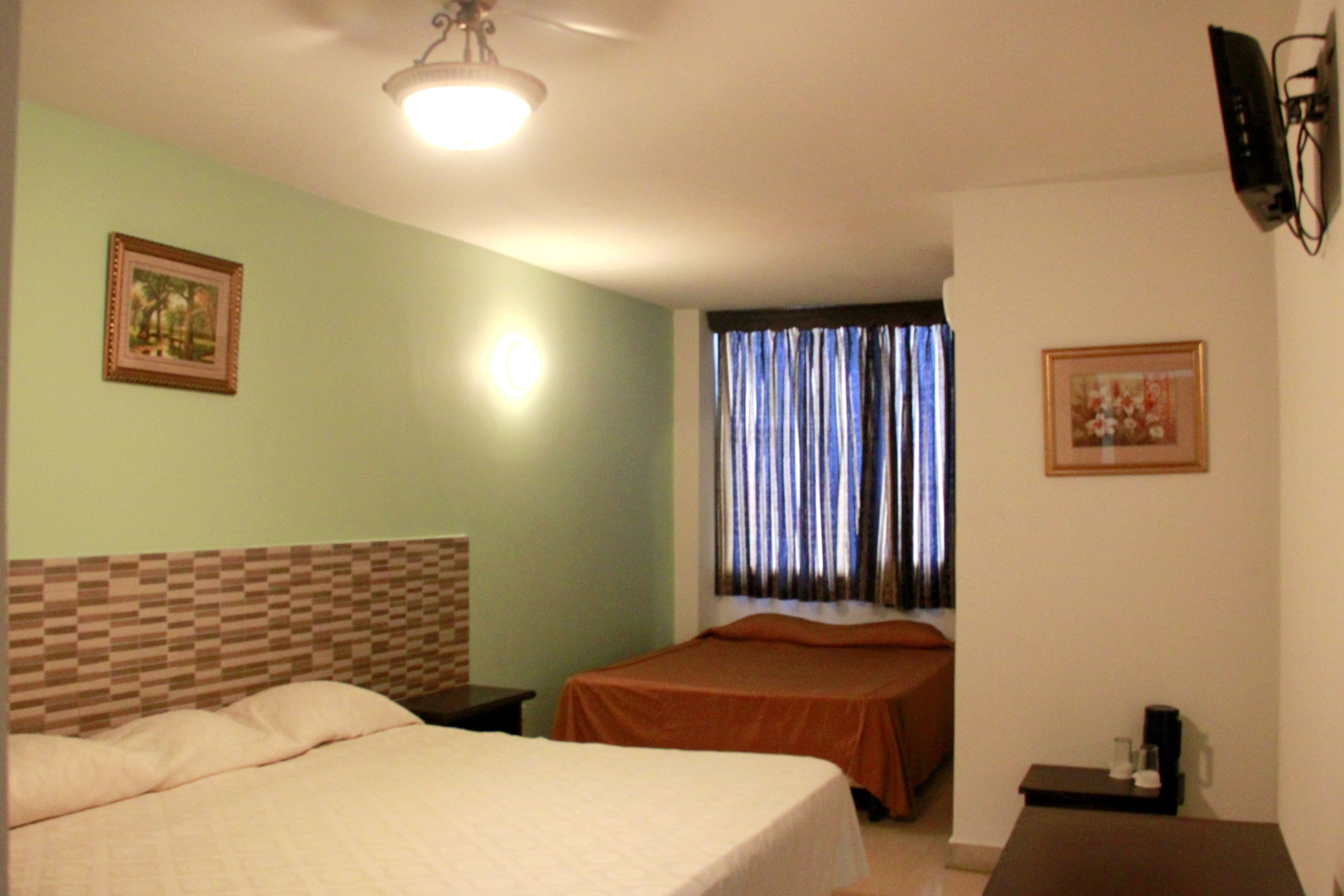 A hotel room with two beds, a headboard with a checkered pattern, a ceiling light, and a window with curtains.