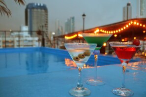 Three martini glasses on a blue surface with a cityscape and string lights in the background. - Hotel Caribe (Panama City)