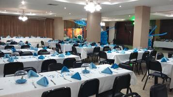A banquet hall with multiple round tables set for a formal event, featuring blue napkins and clear glassware.
