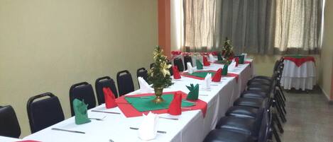 A conference room with a long table set for a meeting, chairs aligned along the walls, and a small Christmas tree centerpiece.