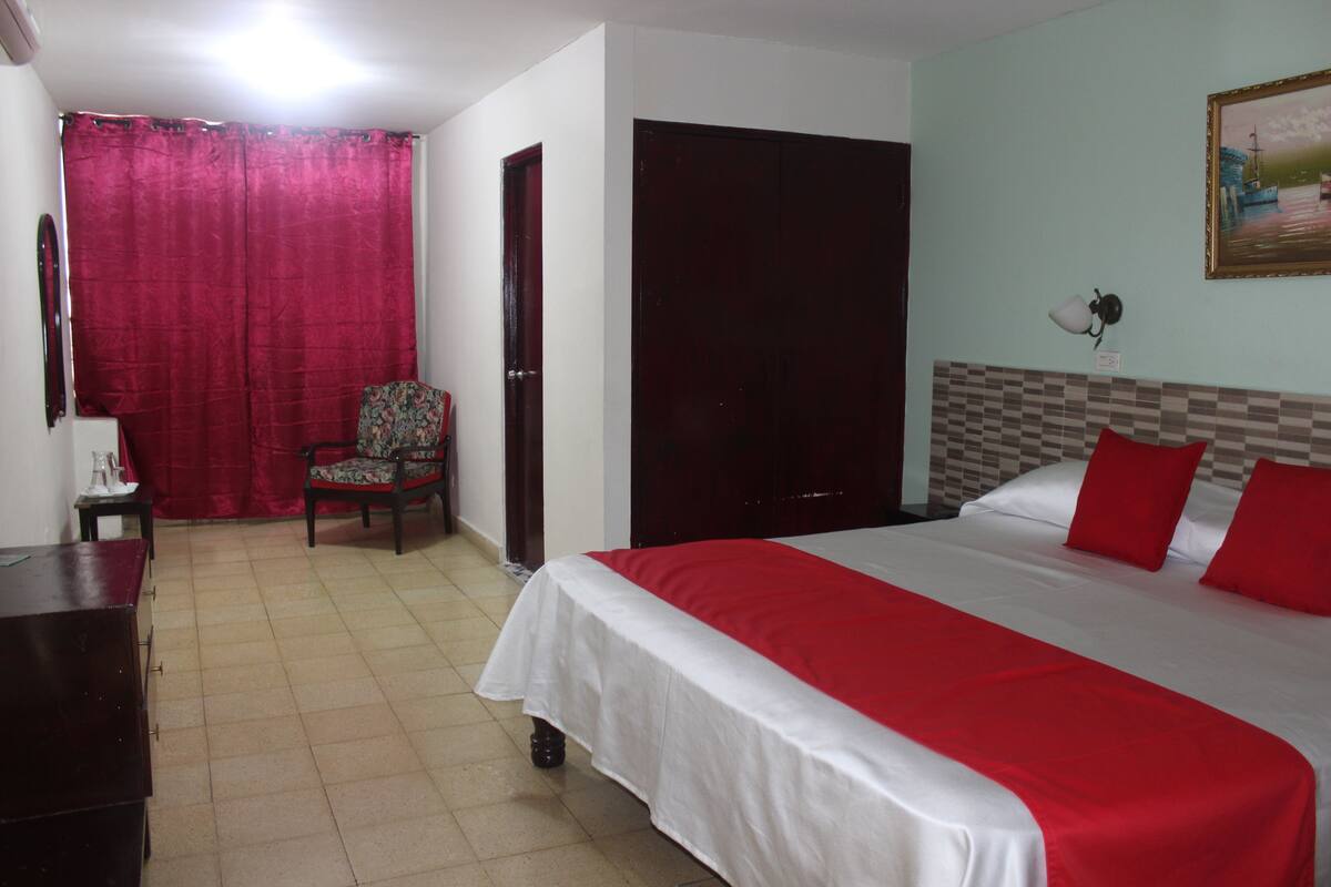Una habitación de hotel con cama, sillón, escritorio y armario.