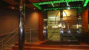 Entrada de un hotel con puerta de cristal, escalera de metal e iluminación verde.