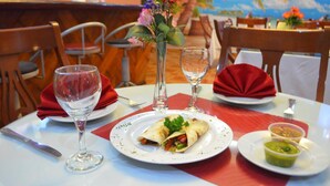 Una mesa de comedor con un plato de comida, un vaso de agua y un jarrón con flores.