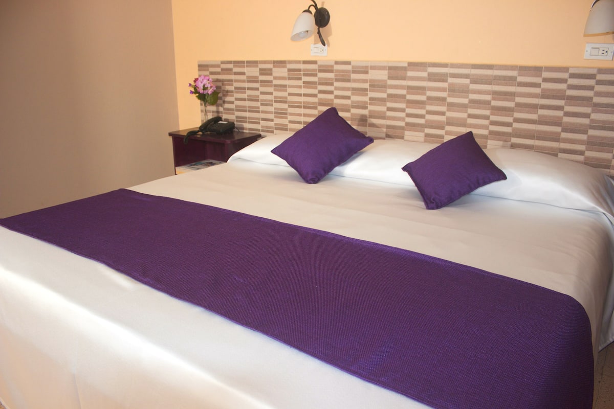 Habitación de hotel con una cama grande, una mesita de noche con teléfono y una lámpara de pared.