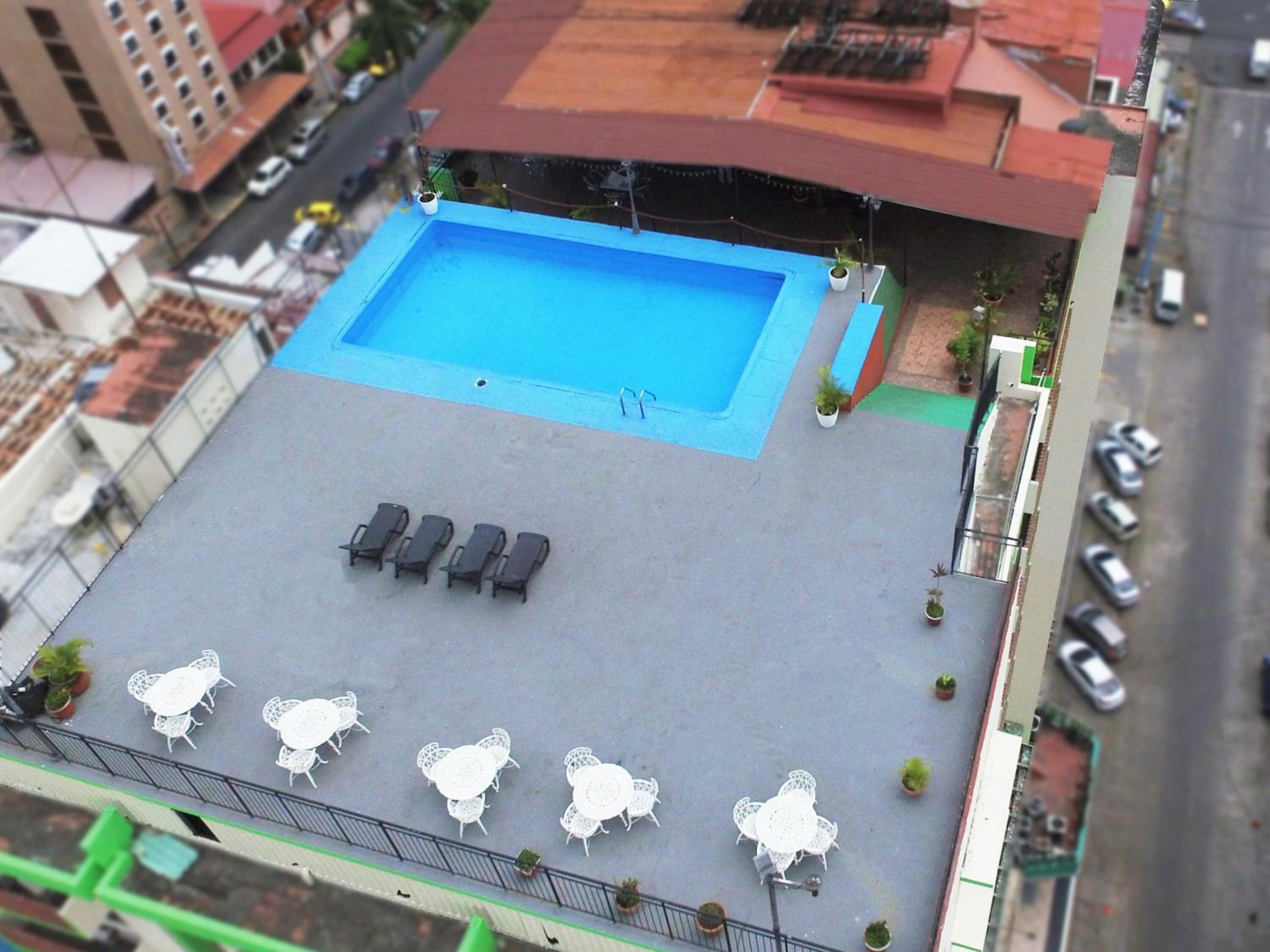 Une piscine sur le toit, agrémentée de chaises longues et de tables, entourée d’une clôture et de plantes en pot.