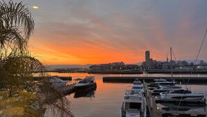 A marina with boats docked, a city skyline in the background, and a sunset over the water. - Hotel Marinoa Resort Fukuoka (Fukuoka)