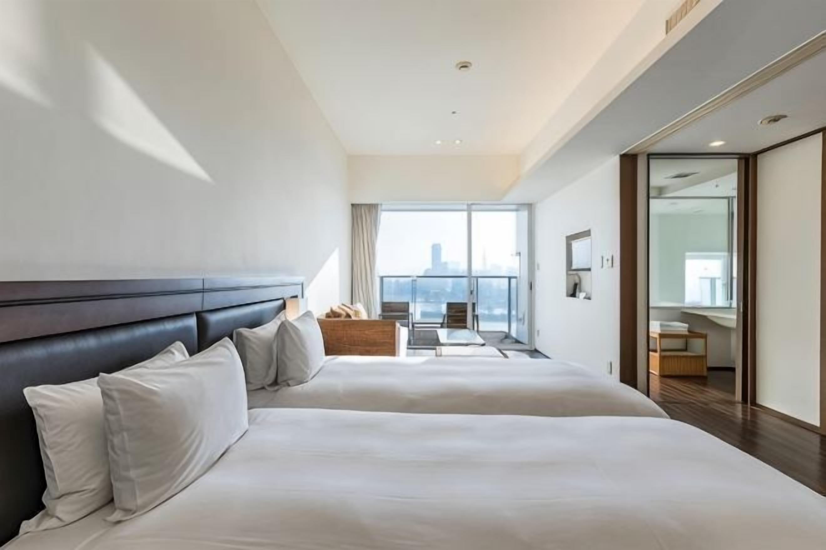 A hotel room with two beds, a balcony, a city view, and a modern design.