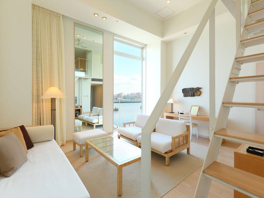 Una habitación de hotel moderna con un sofá, dos sillones, una mesita, un escritorio y una escalera.