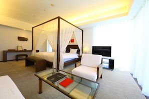 A hotel room with a four-poster bed, a glass coffee table, a TV, and a seating area with a chair and ottoman. - Hotel Marinoa Resort Fukuoka (Fukuoka)