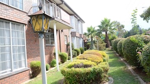 A brick building with a balcony, a well-maintained garden with hedges and a palm tree, and a street lamp. - Motel Margeurita (Queanbeyan)
