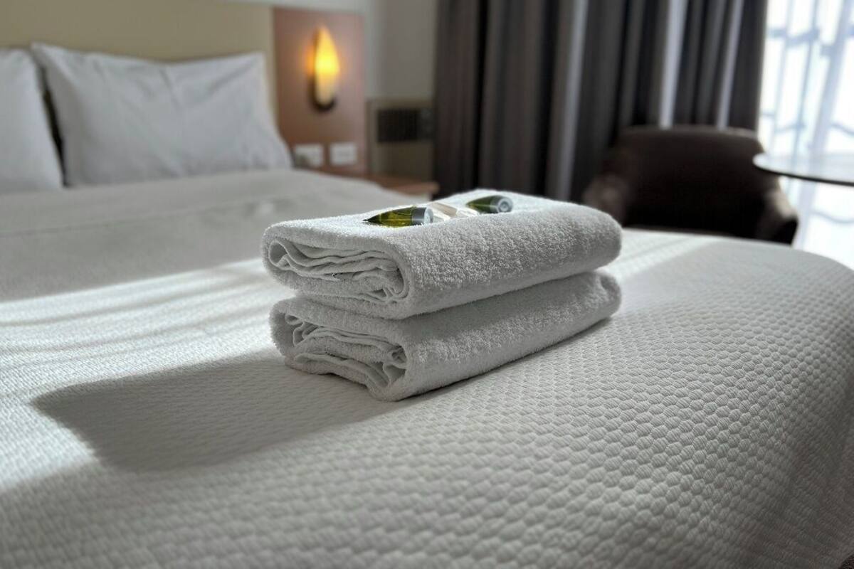A neatly made bed with folded white towels and a decorative item on the bed.
