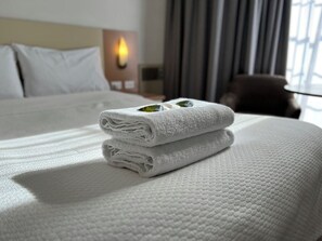 A neatly made bed with folded white towels and a decorative item on the bed. - Motel Margeurita (Queanbeyan)