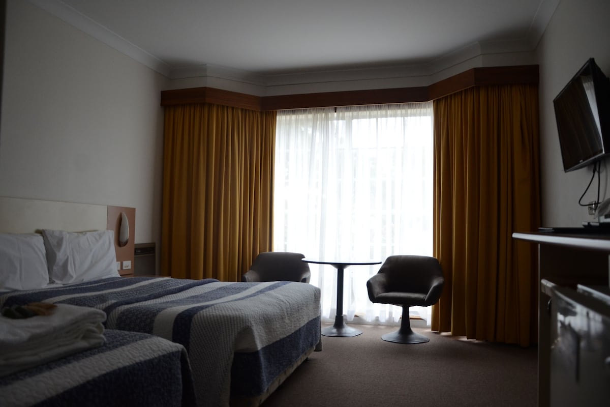 Ett hotellrum med en säng, två fåtöljer, ett litet bord och en tv.