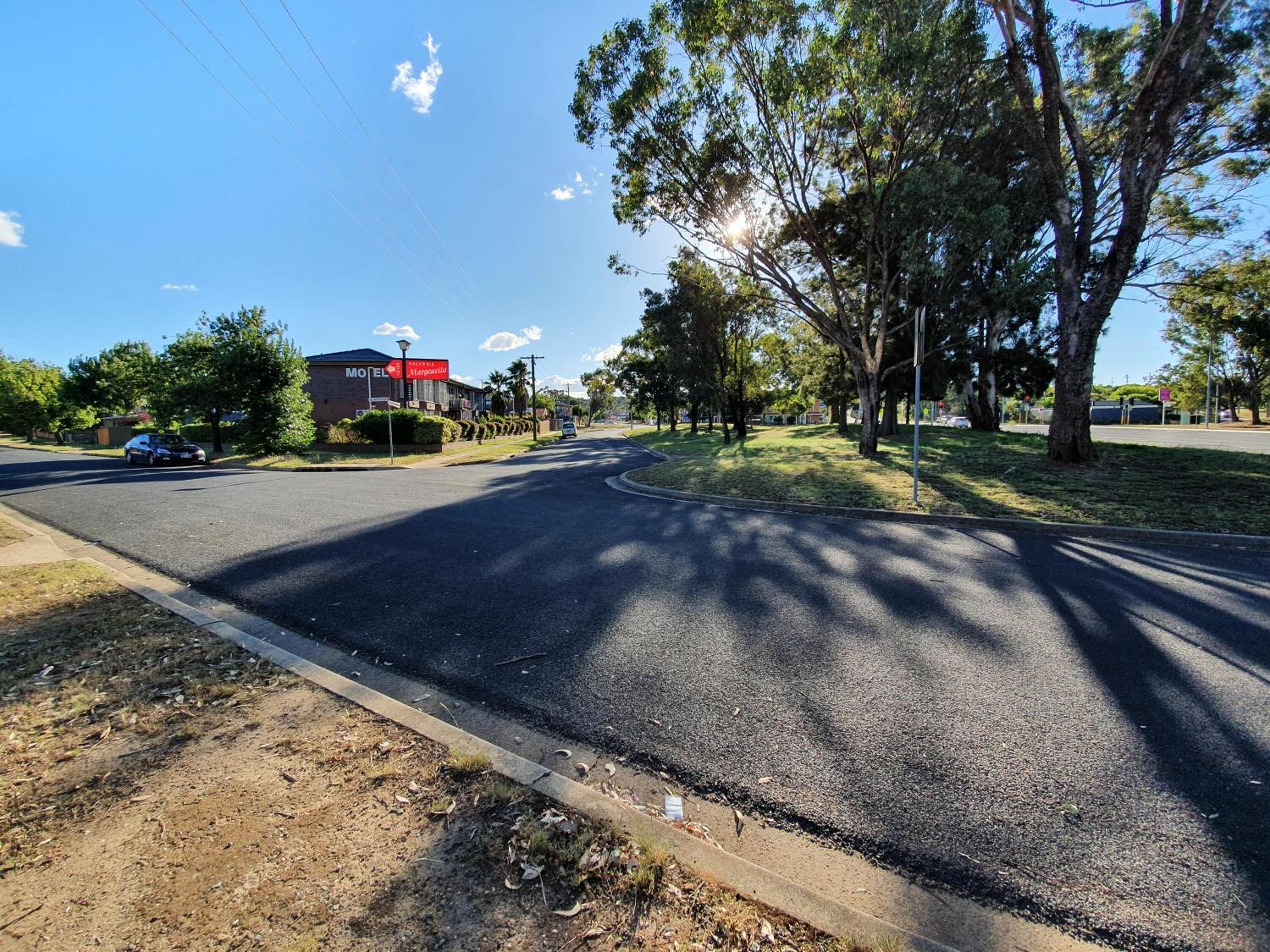 A road leading to a motel with a red sign, surrounded by trees and a clear sky.