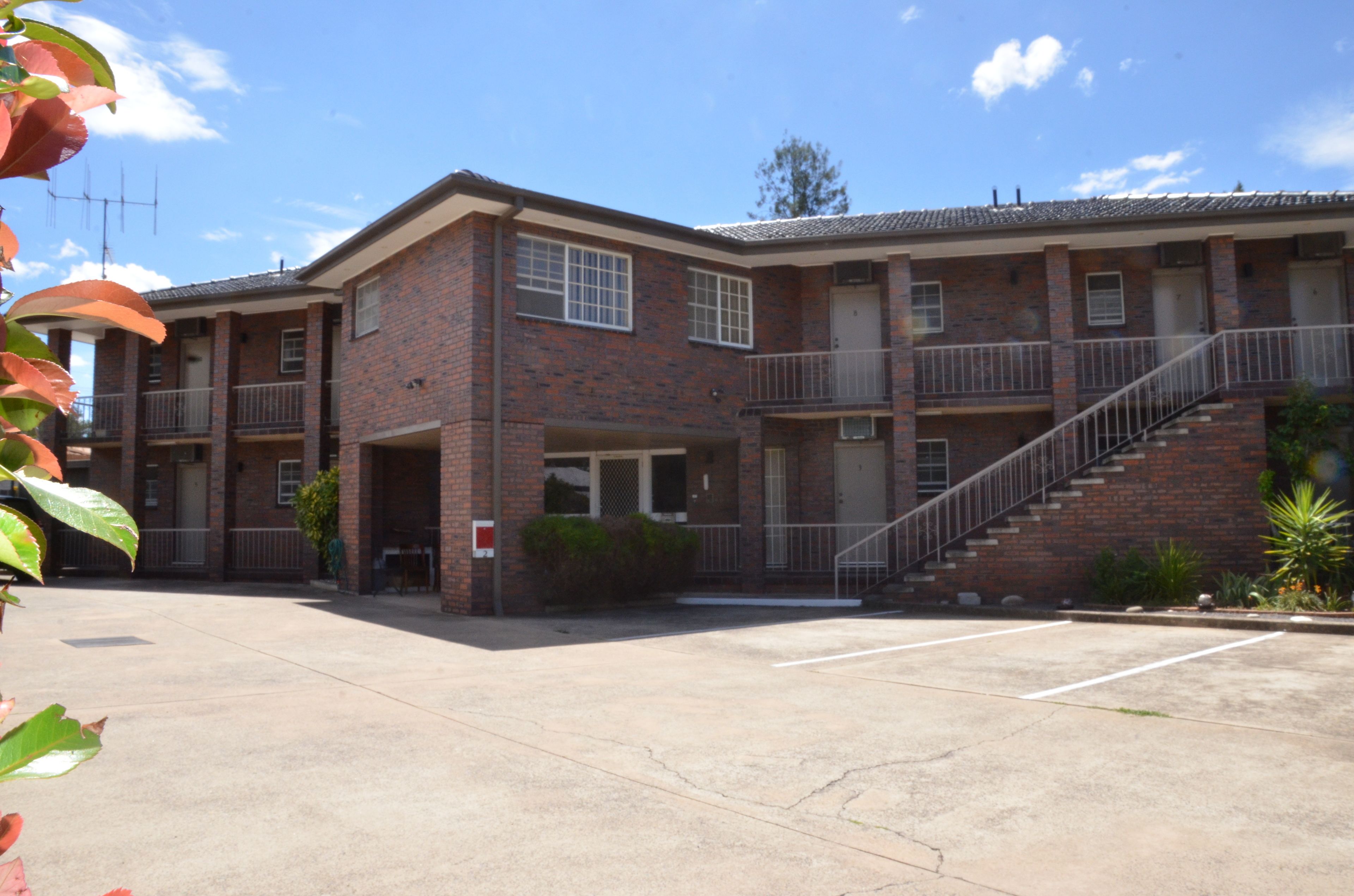 A two-story brick building with a central entrance, a covered outdoor area, and a staircase leading to the upper floor.
