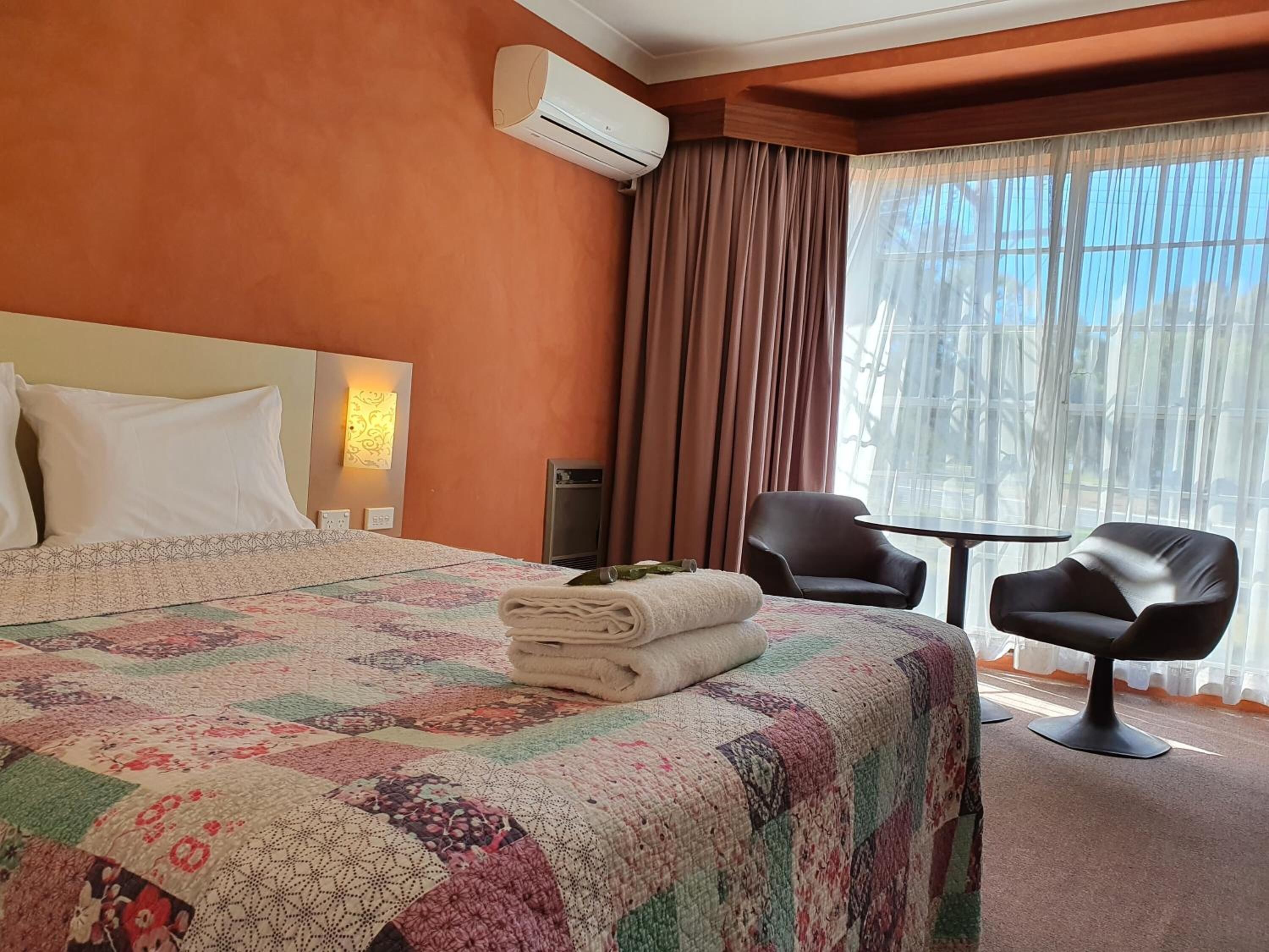 Une chambre d’hôtel avec un grand lit, un bureau, deux chaises, un appareil de climatisation et une fenêtre avec des rideaux.
