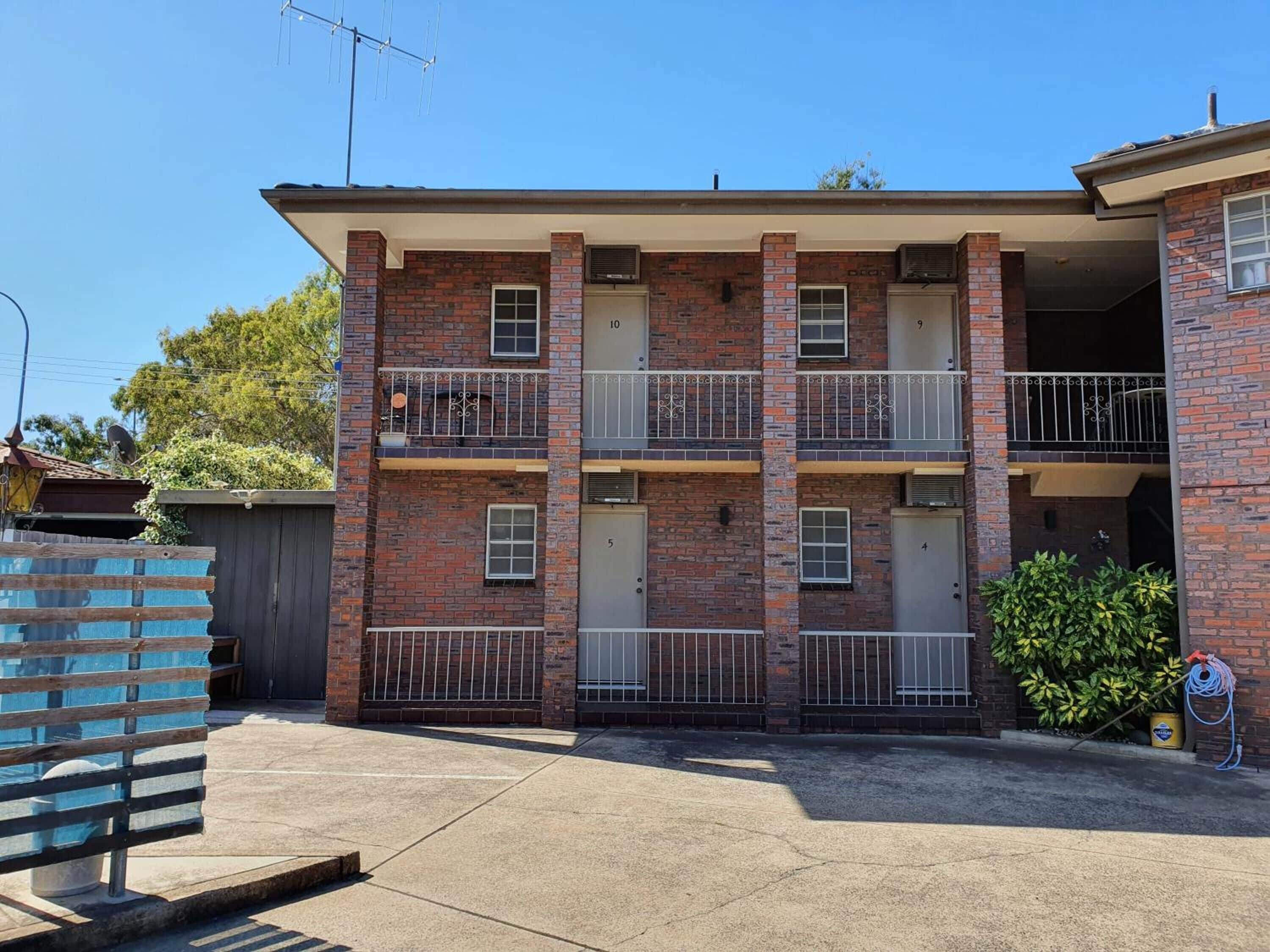 A multi-story brick building with numbered doors, balconies, and a visible satellite dish.