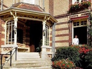 A building with a stone facade, a wooden porch with a roof, and a person standing at the entrance.