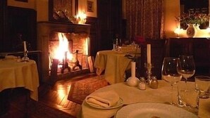 A warmly lit dining room with a fireplace, tables set for a meal, and a cozy atmosphere. - Château de la Rapée (Bazincourt-sur-Epte)