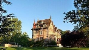 A large, historic building with a prominent tower and multiple windows, surrounded by a well-maintained lawn with a few lounge chairs. - Château de la Rapée (Bazincourt-sur-Epte)