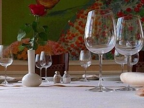 A dining table set with wine glasses and a vase with a red rose.