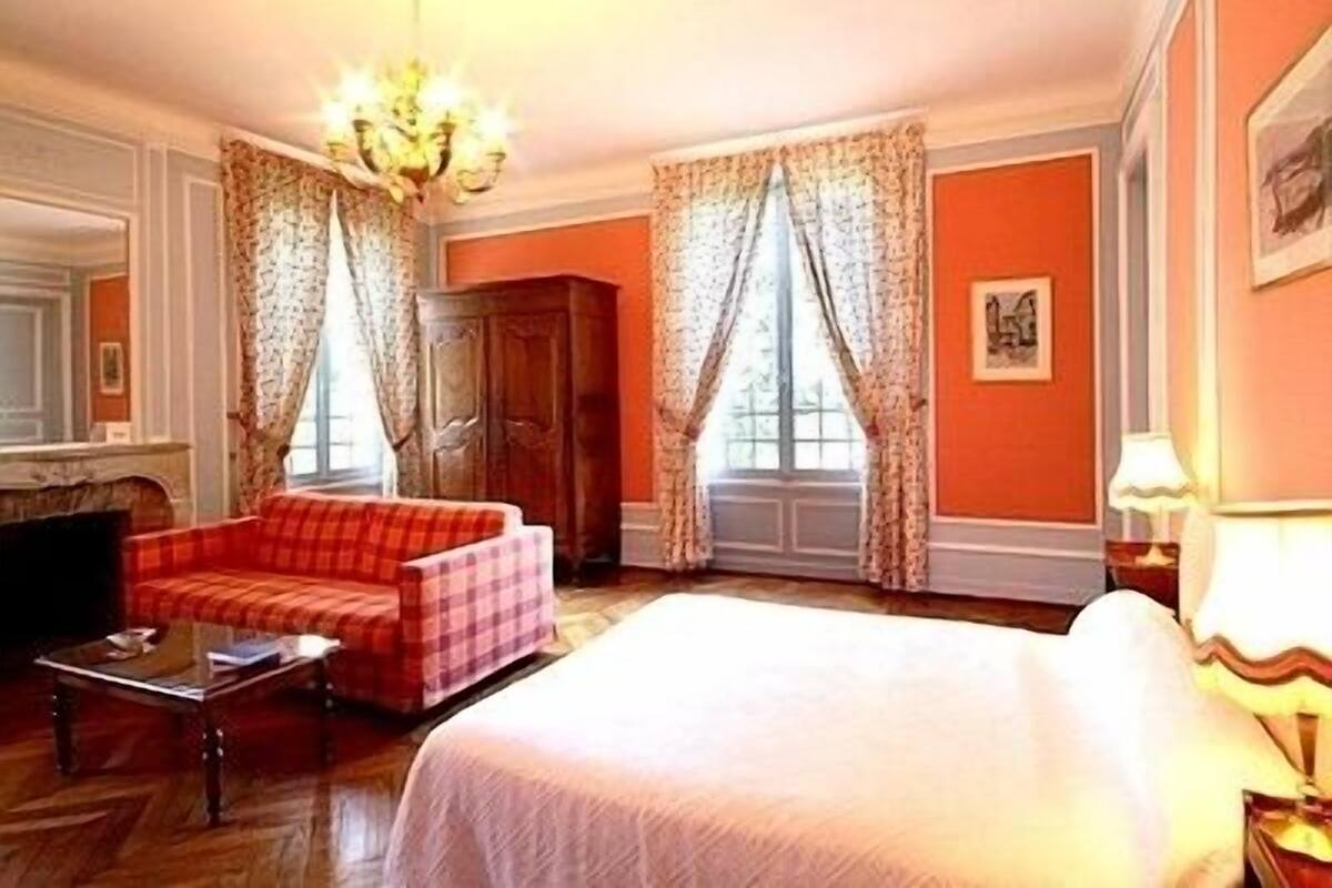 Ett hotellrum med en stor säng, en röd, rutig soffa, en garderob i trä och en kristallkrona.