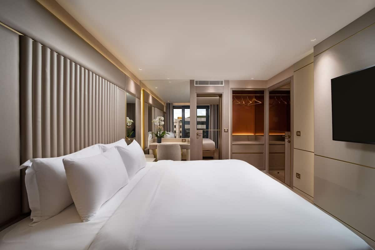 A modern hotel room with a large bed, a desk, and a walk-in closet.
