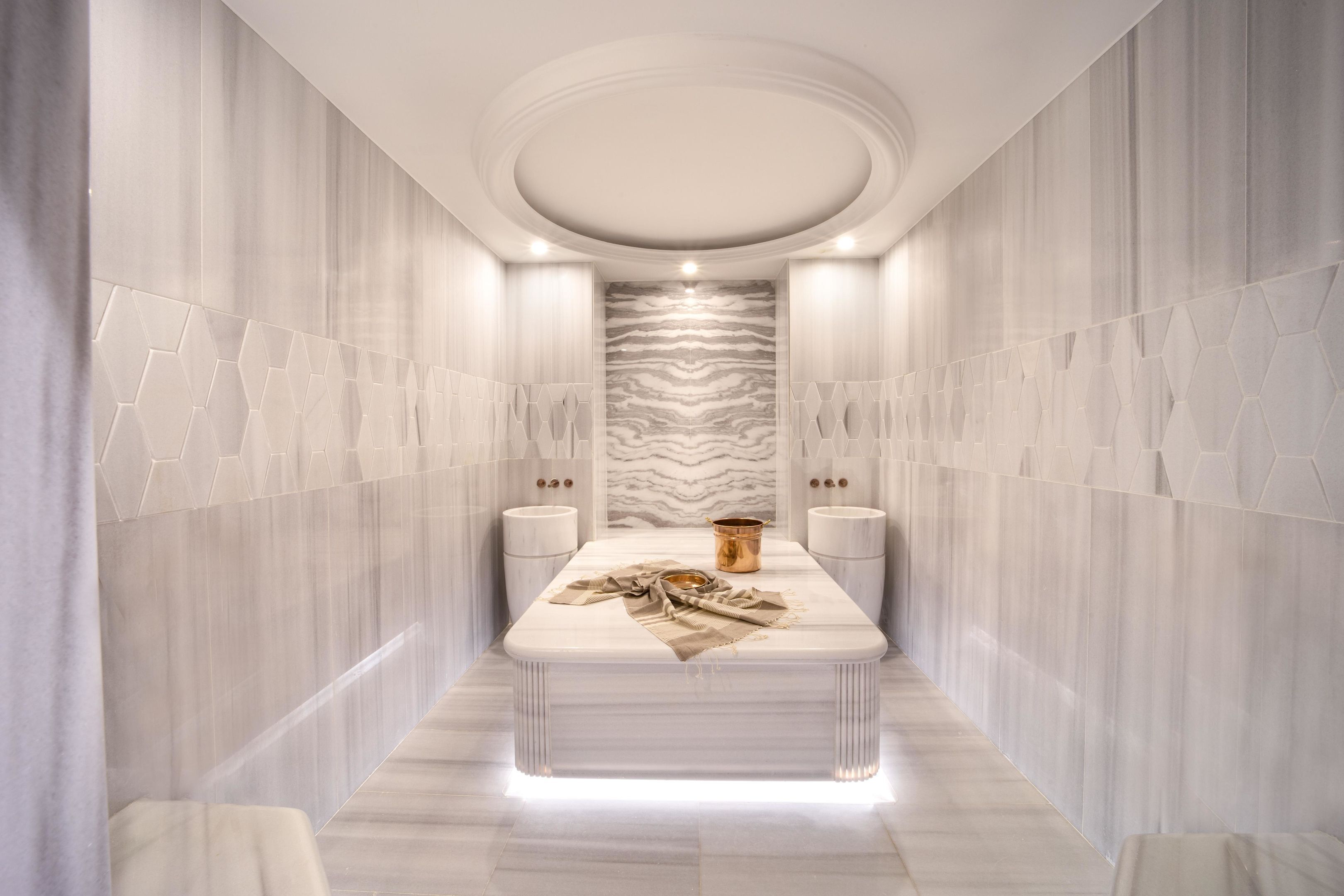 A modern, well-lit hallway with a marble floor, a central table with a cloth, and a patterned wall.