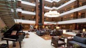 Een ruime lobby met een vleugelpiano, comfortabele zithoeken en een moderne kroonluchter.