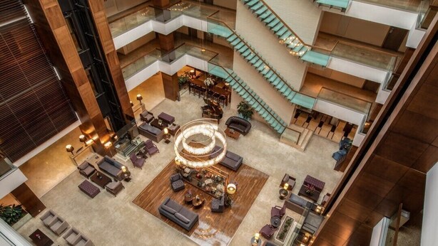 Een meerlaagse hotellobby met een centraal zitgedeelte, meerdere balkons en een spiltrap.