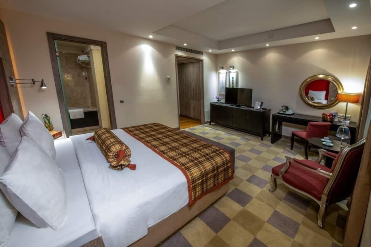 A hotel room with a bed, a desk, a TV, a mirror, and a chair.