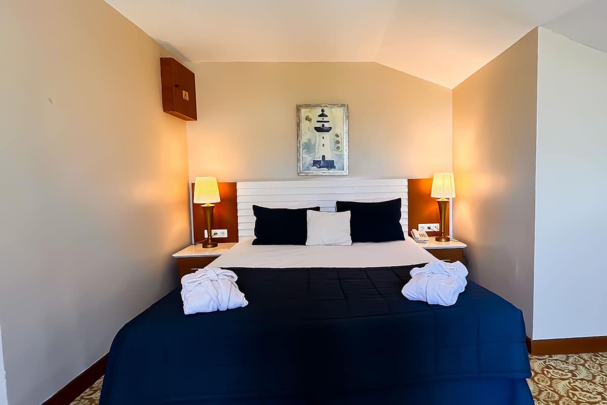 A hotel room with a bed, two bedside lamps, a framed picture on the wall, and a small cabinet.