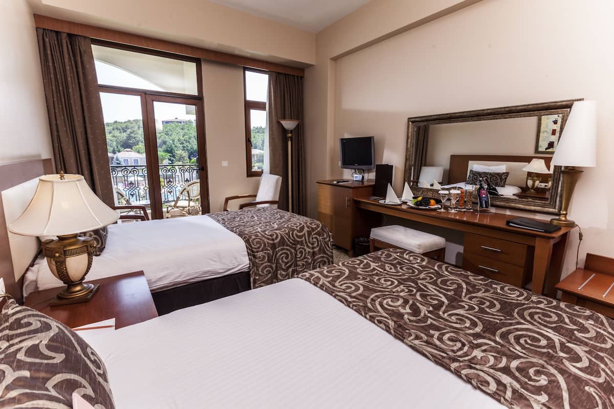 A hotel room with two beds, a desk with a computer, a chair, a large mirror, and a balcony view.