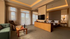 A hotel room with a sofa, a dining table with a bottle and glasses, a TV, a bed, and a bedside table with a lamp. - The Sign Şile Hotel & Spa (Sile)